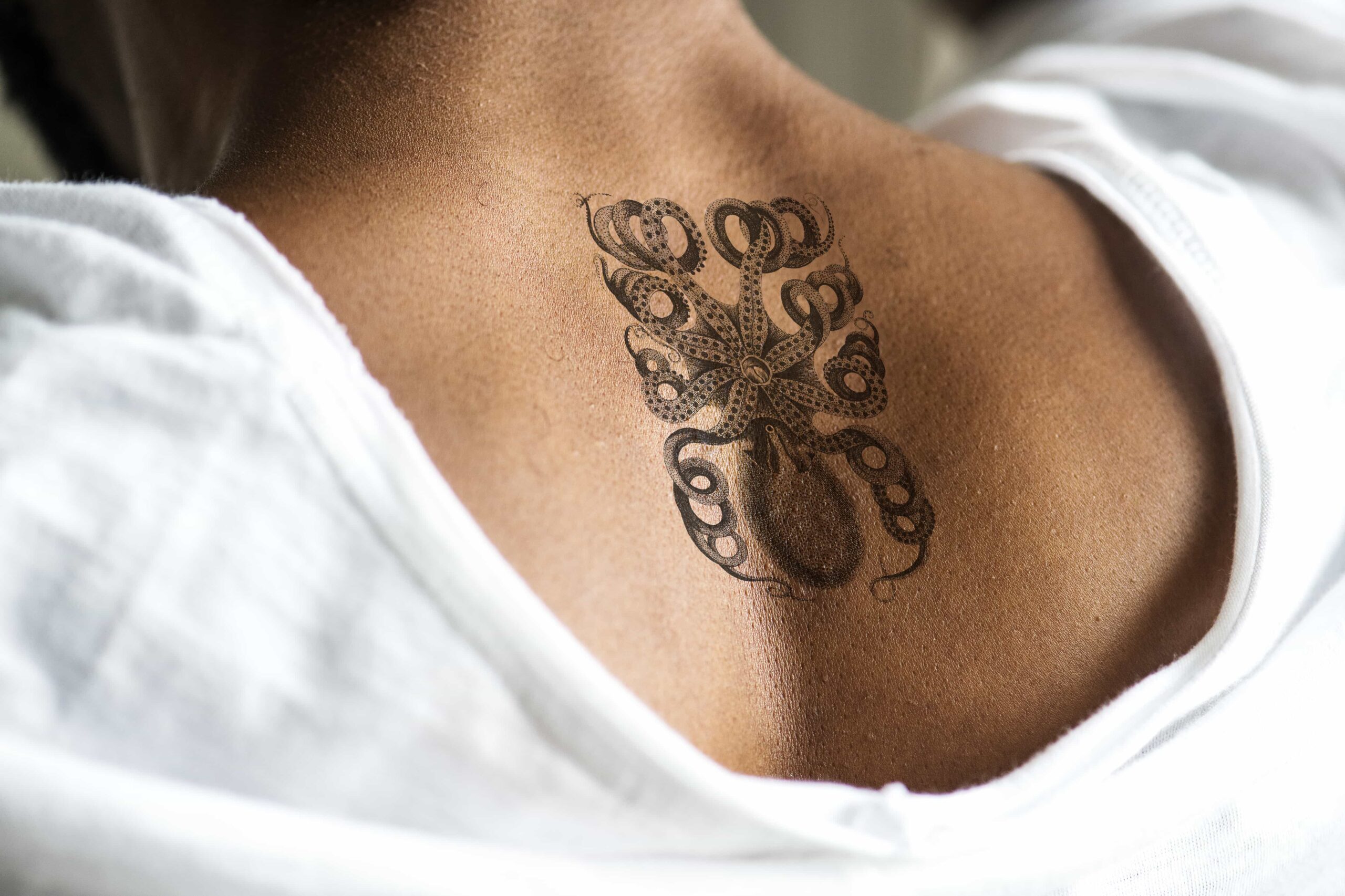 Black and white ornamental octopus tattoo centered on a person's upper back and shoulders.