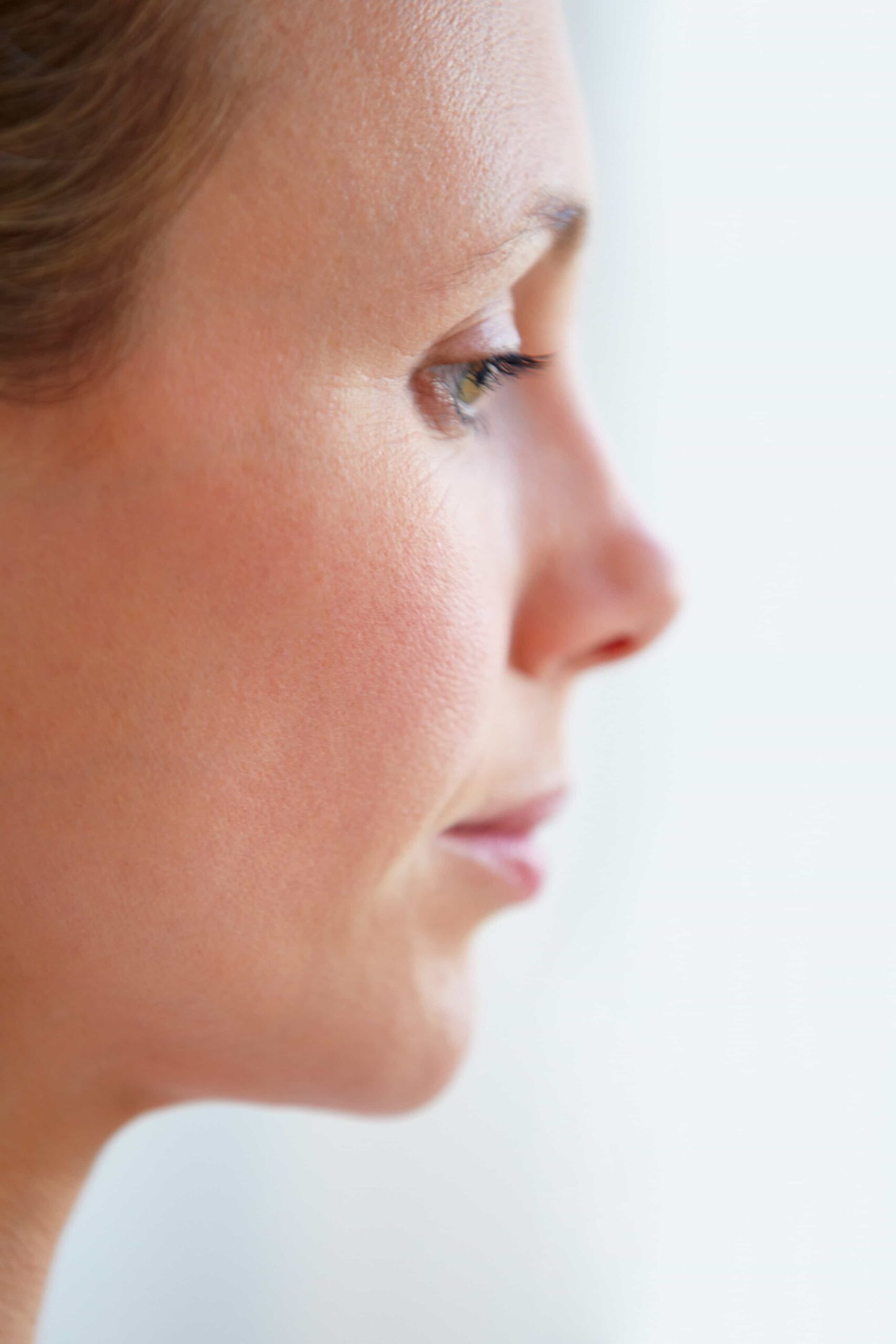 Profile view close-up of a woman's face, focusing on the natural shape of her nose and cheek against a bright white background.