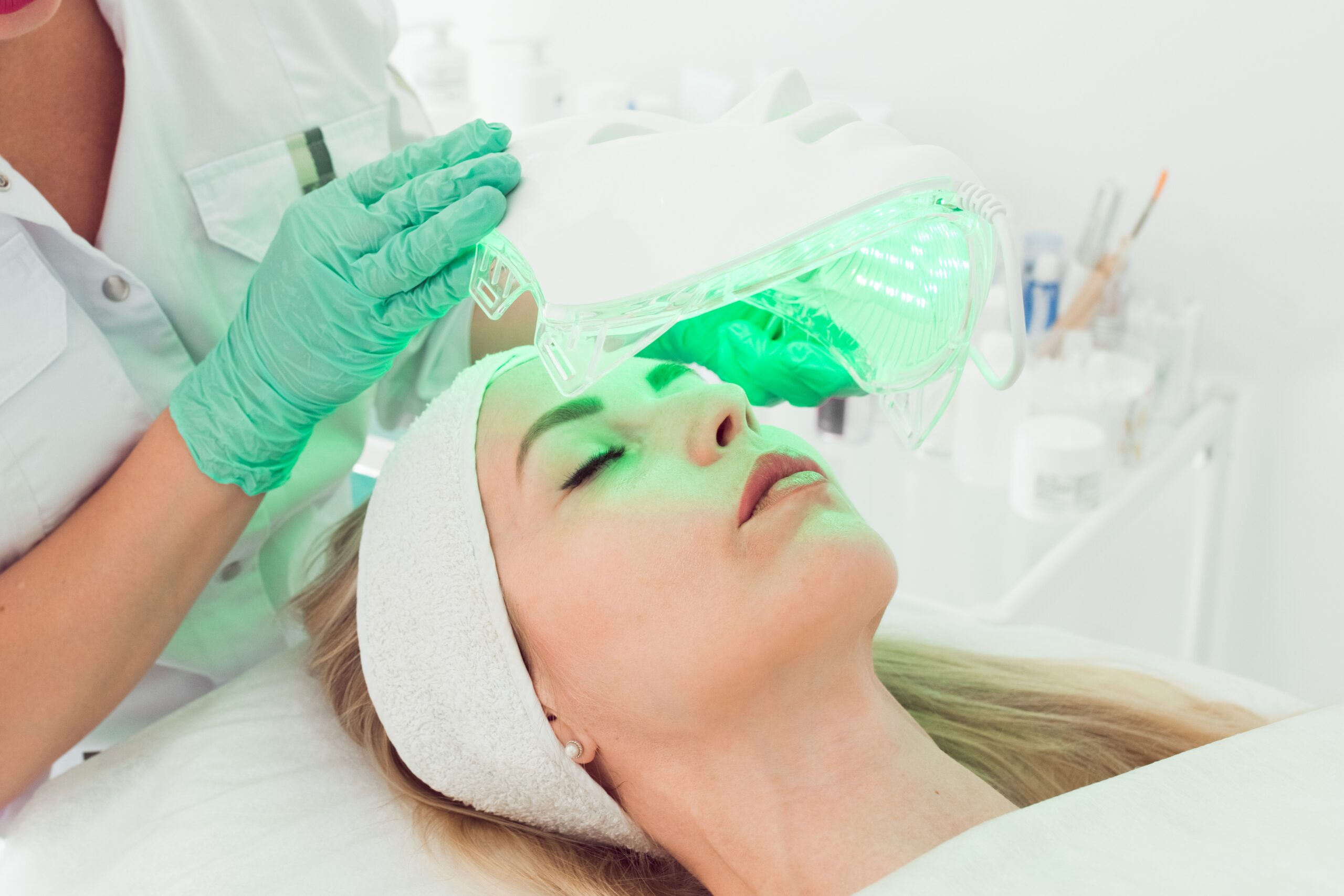 cosmetologist applying light therapy led facial 